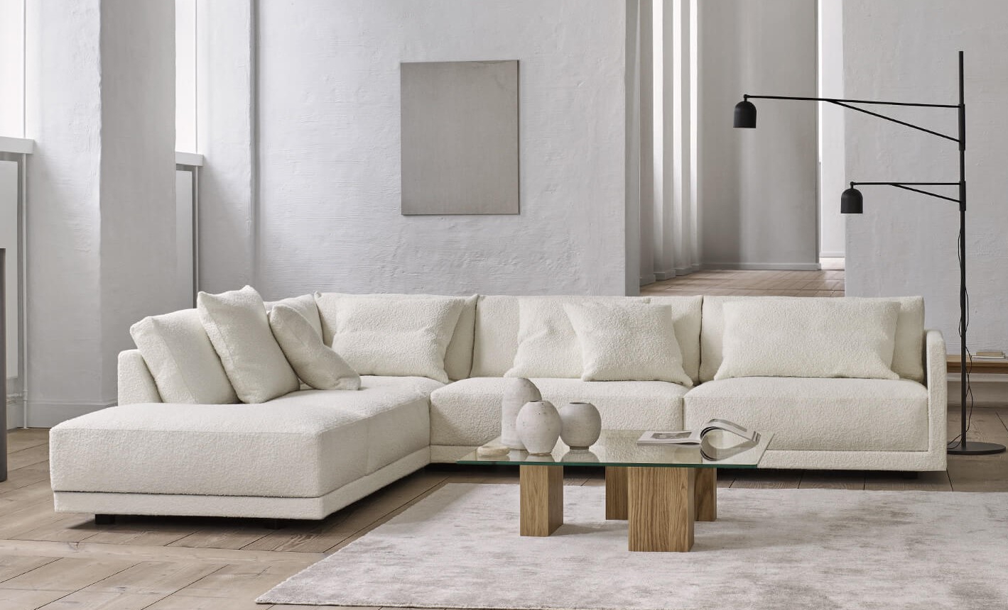 Eilersen Drop Corner Sofa in white boucle fabric styled with a glass and oak coffee table in a minimalist living room