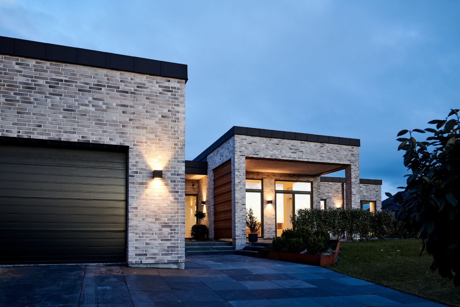 Light-Point Copenhagen CUBE Up Down LED XL wall light in black, casting symmetrical light patterns on a contemporary brick fa&ccedil;ade at dusk.