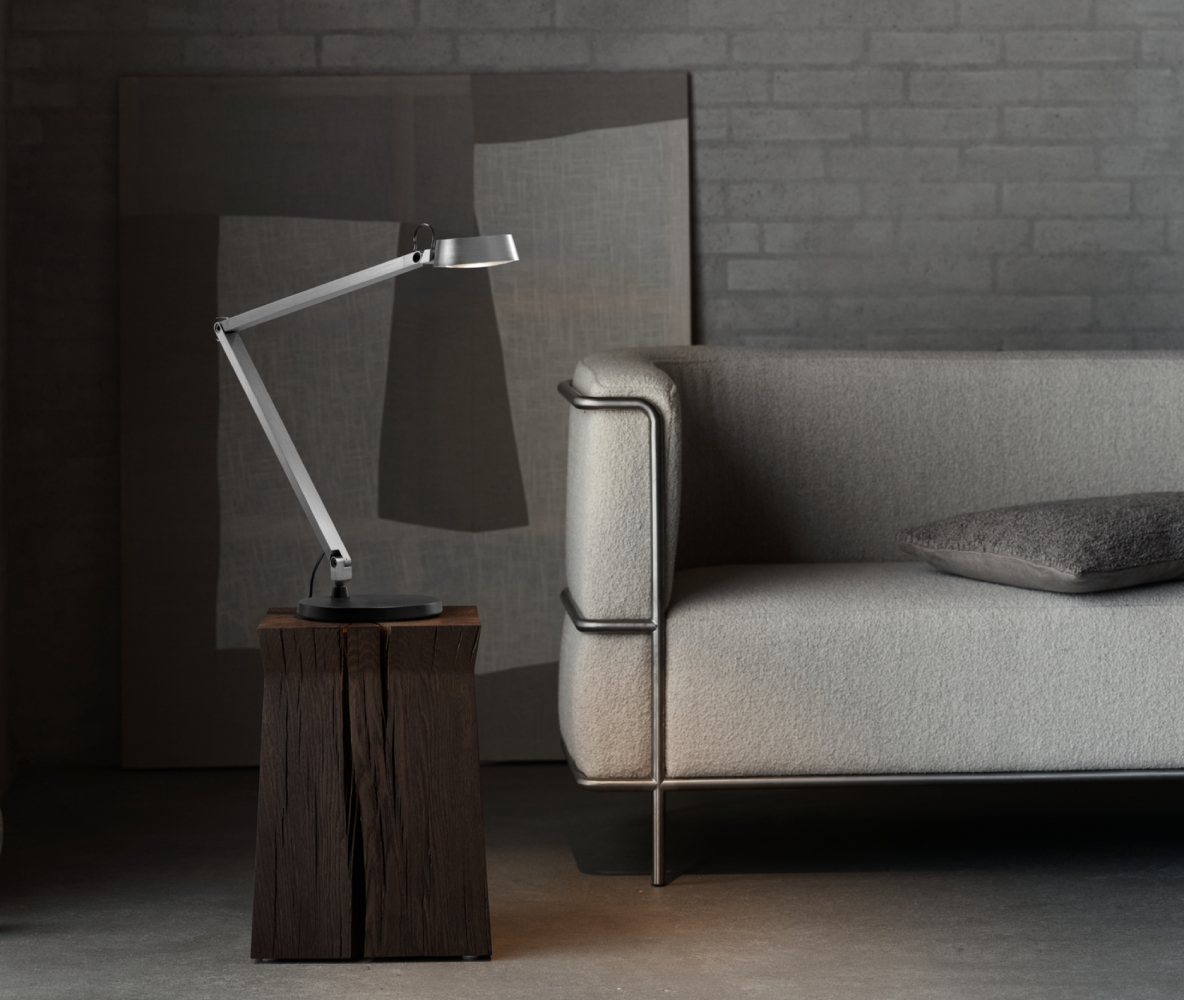 Light-Point Copenhagen DARK T1 table lamp in titanium, featuring an adjustable arm and focused task lighting beside a modern sofa in a refined interior setting.