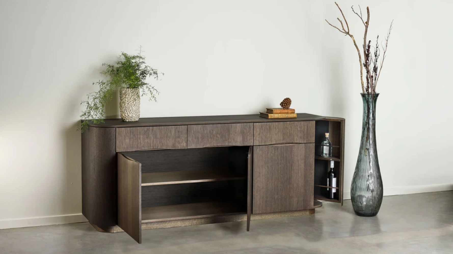 Walnut Collum sideboard with open shelving and storage compartments styled indoors with decorative vases, books and houseplants against a neutral wall.