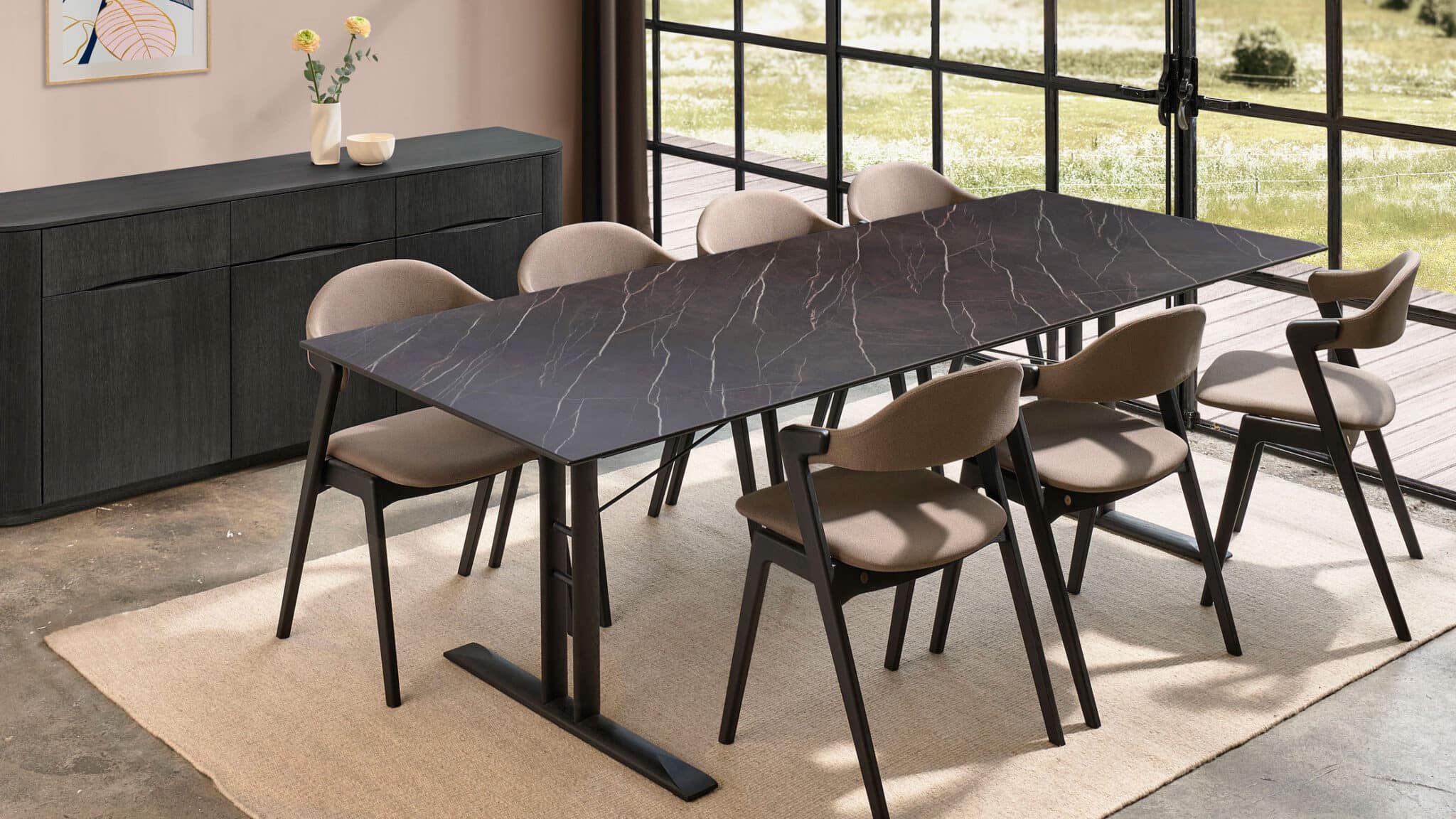 Minimalist indoor dining scene featuring a rectangular dark stone dining table with six upholstered dining chairs beside large industrial-style windows.