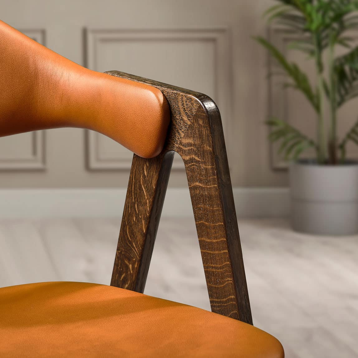 Close-up detail of a Titan dining chair showing smoked oak timber frame and curved cognac leather seat and backrest in an indoor setting